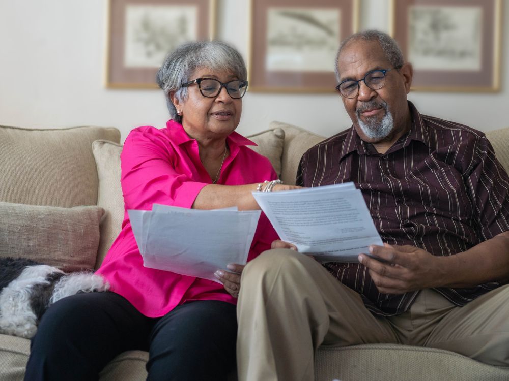 Casal analisando documentos no sofá, representando a revisão de contratos e informações sobre o pagamento antecipado de planos de saúde."